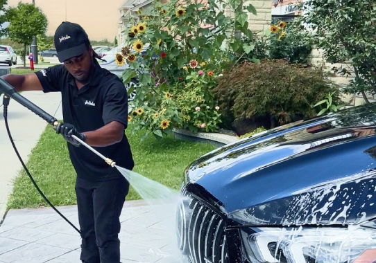 Professional mobile car detailer from Panda Hub, pressure washing the hood of a black car with soap foam during exterior detailing and car wash