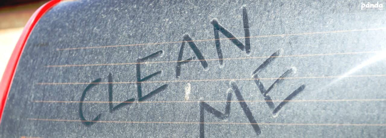A dusty rear car window with "CLEAN ME" finger-written in the grime.