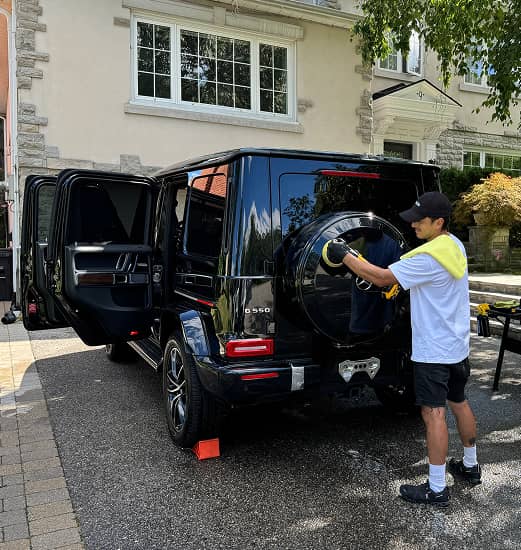 Professional detailer polishing the rear of a black Mercedes G-Class SUV