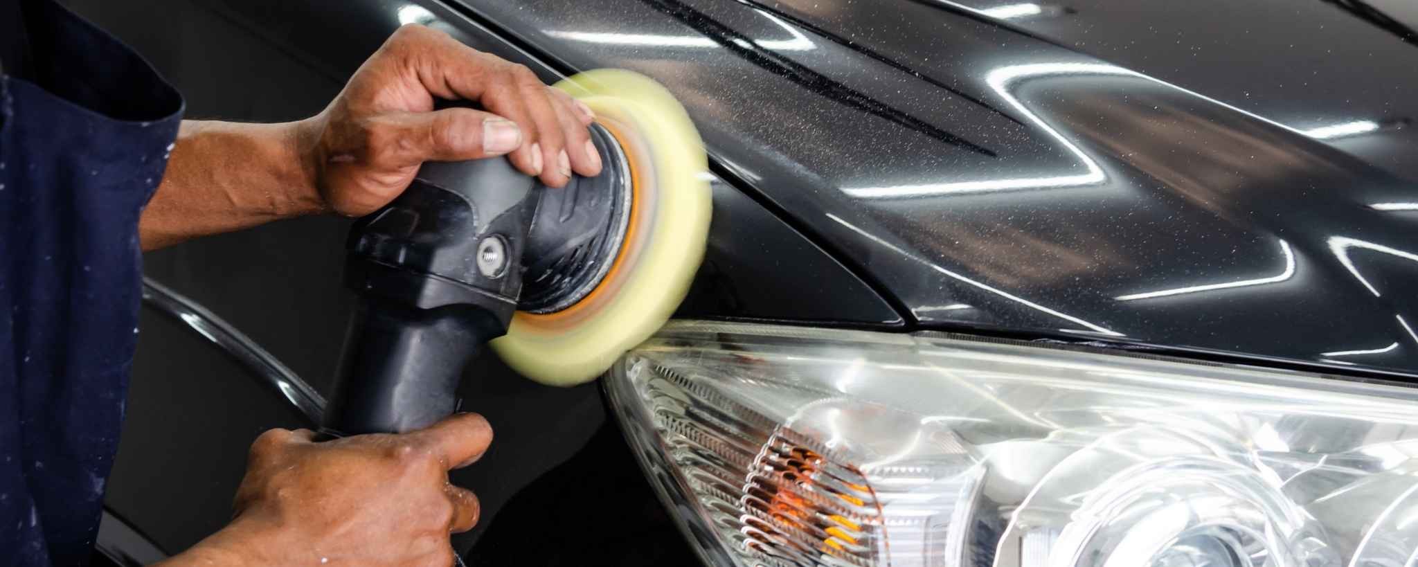 Car detailer polishing a black vehicle near the headlight using a power buffer for paint correction