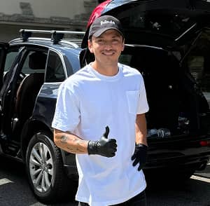 Smiling Panda Hub car detailer wearing gloves and cap giving thumbs up in front of SUV during mobile detailing service